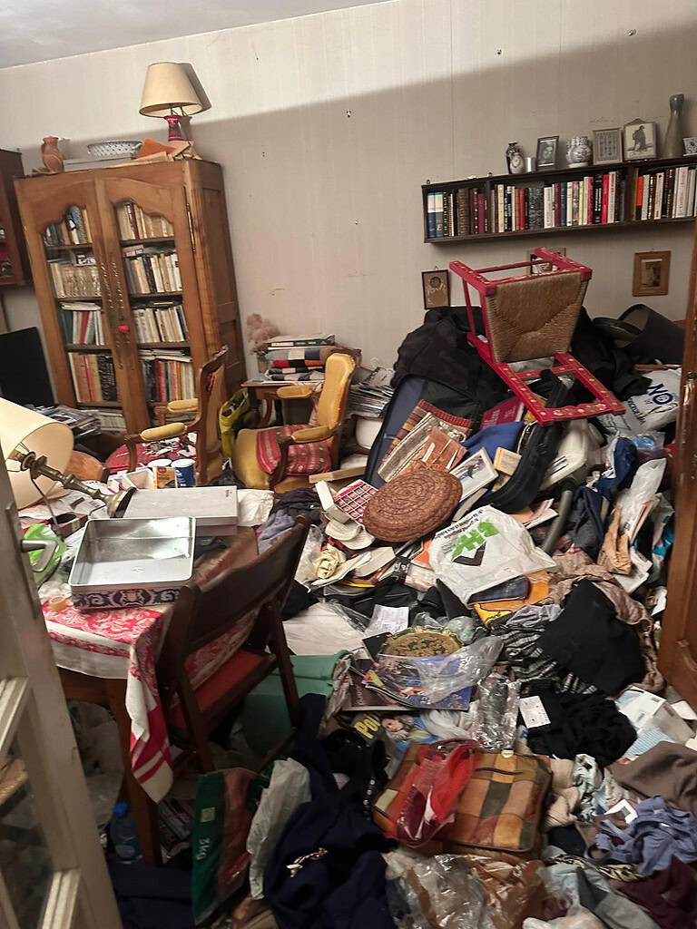Désordre intérieur avec meubles, livres, vêtements et objets divers en désordre.